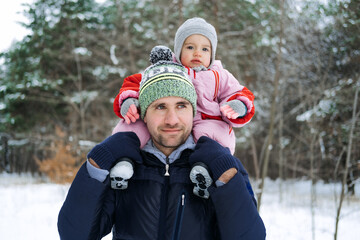 Fototapeta na wymiar Portrait of happy father and baby toddler daughter on winter nature background. Man and baby girl on his shoulders in winter park. Christmas holidays, Family vacation in winter forest.