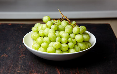 Branch of ripe green grape on plate. Juicy grapes on wooden background, closeup. Grapes on dark kitchen table with copy space