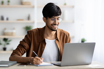 Handsome arabic guy employee surfing on Internet and taking notes
