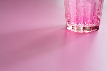 Glass of pink bubbly drink on pink background