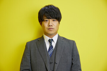 黄色い背景の前で爽やかに笑うスーツを着た日本人男性	