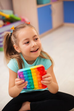 A girl plays on the floor in the children's room with the popular pop it toy. A toy for the development of motility.Development of fine motor skills. A child holds a popit toy in his hands. 
