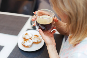 A young girl drinks black coffee from a transparent mug for breakfast and eats cakes, top view.
