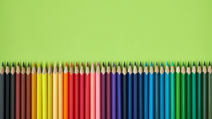 Colored pencils in a row on green background