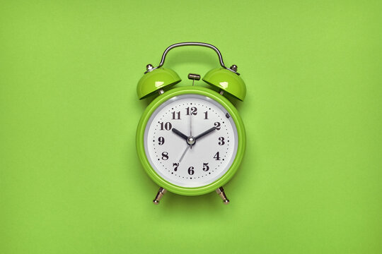 Green alarm clock on light green background