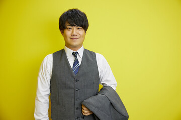 黄色い背景の前で爽やかに笑うスーツを着た日本人男性	