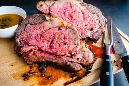 Slices of Medium Rare Bone-in Prime Rib with Au Jus: Carved standing prime rib roast on a bamboo carving board