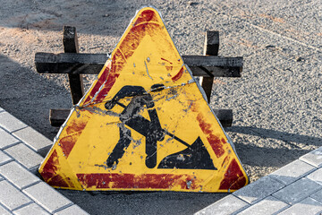Old dented road works sign. Fencing the hazardous area where repair work is underway.