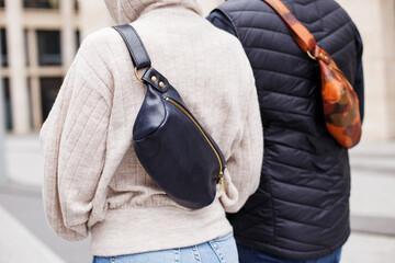 A man and a woman are holding their new banana bags in the city. Brown and black bags for men and women made of genuine leather. Leather Hip Bag Over the Shoulder Waist Bag made of genuine leather.
