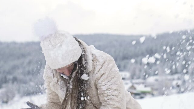 Young beautiful woman is spinning, and someone is sprinkling snow on her. Winter fun.
