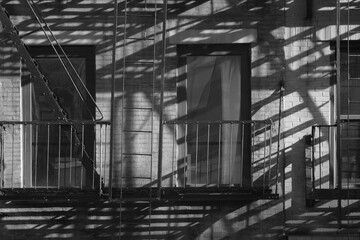 New York City tenement style apartment building windows with fire escape casting long intricate shadows or the early morning sunlight  - obrazy, fototapety, plakaty