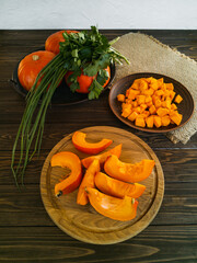 Orange little pumpkins for cooking dishes and recipes on a wooden board and a dark table, cut into pieces