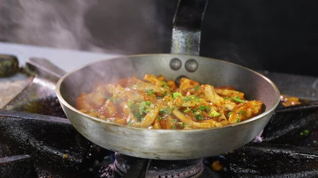 Making fried pork Brasso style - adding herbs to the meat in a pan, tossing and turning