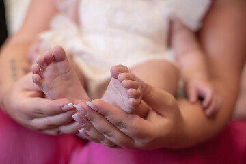 Delicate baby girl's bare feet held my her mother's beautifully manucured hands or an affectionate...
