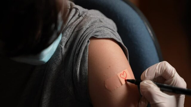 Closeup suggestive shot of a doctor drawing a red heart on the patch of a boy with a surgical face mask after giving the Covid-19 vaccine shot.