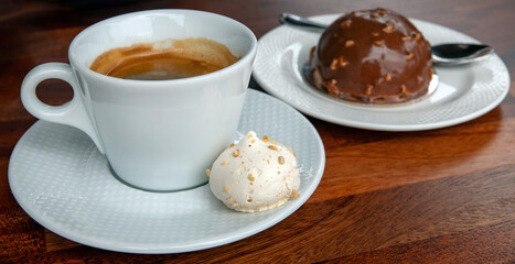 Delicious caffee americano with a sweet meringue aside and a small chocolate and nuts dome cake,...