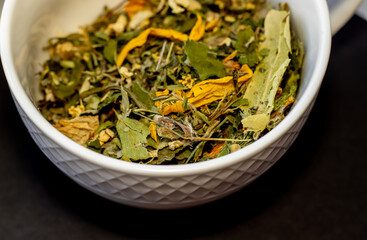 herbal tea leaves on black background or in white ceramic cup.tea from natural herbs harvested in own garden,natural, eco,ecological product.top view.night tea for insomnia,calm,relaxation,bio leaves.