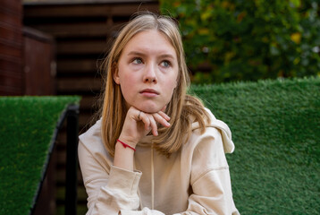 sad pimply teenager sitting on a bench in the park alone. Looking away from camera.
