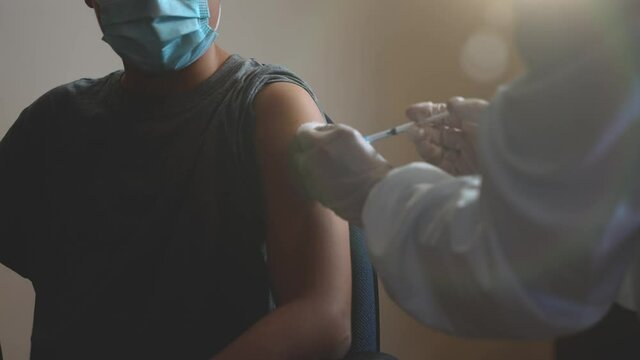 Suggestive shot of a boy with a surgical face mask getting the Covid-19 vaccine shot. A child having his dose of Coronavirus vaccine. Sun through the window.