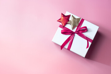 White gift box with bow on pink background with star decor, christmas day present. A box for surprise in holiday.