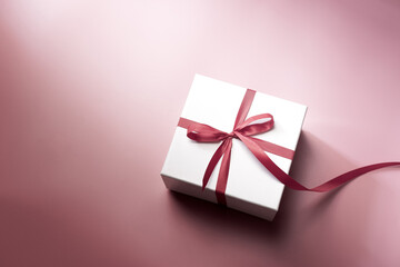 White gift box with red ribbon on pink background, christmas day present. A box for surprise in holiday.