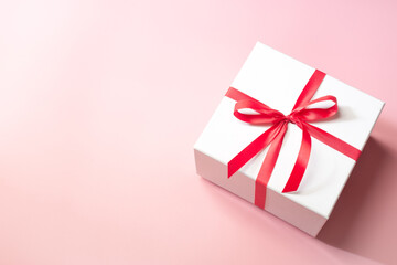White gift box with red ribbon on pink background, christmas day present. A box for surprise in holiday.