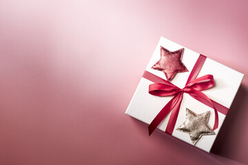 White gift box with red ribbon on pink background, christmas day present. A box for surprise in holiday.