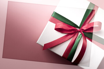 White gift box with red and green ribbon on pink background, christmas day present. A box for surprise in holiday. White frame for text.