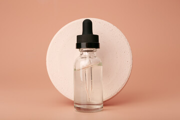 Skin serum or oil in transparent glass bottle with round gypsum circle against beige background