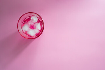 Glass of pink bubbly drink on pink background, top view