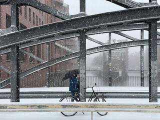The Speicherstadt with the Poggenmühlen-Bridge in Hamburg on a cold winter day with snow flakes in the air and a bicycle