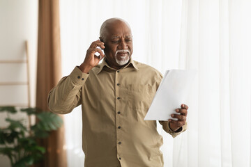 Mature Black Male Talking On Phone Holding Paper Standing Indoors