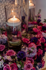 Glass vase of water with burning candle inside decorated by fresh pink and violet roses on table Beautiful glass vase with decor and burning candle Composition with burning candles in vase and flowers