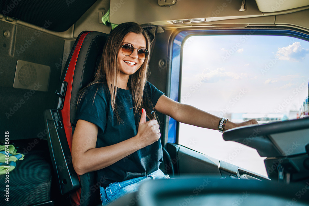 Wall mural portrait of beautiful young woman professional truck driver sitting and driving big truck. inside of