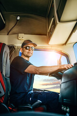 Handsome experienced male truck driver with a hat sitting and driving his truck. Professional...