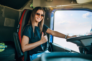 Portrait of beautiful young woman professional truck driver sitting and driving big truck. Inside...