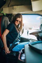 Portrait of beautiful young woman professional truck driver sitting and driving big truck. Inside...