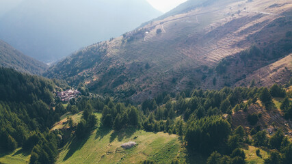 Fototapeta premium Aerial view of green fields and coniferous forest in the mountains. Italian Alps.