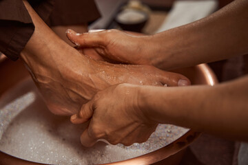 Beauty salon worker rubbing her client feet with sea salt