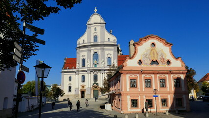 Fototapeta na wymiar altes Franziskanerhaus und schöne Basilika St. Anna mit Menschen im Wallfahrtsort Altötting bei blauem Himmel