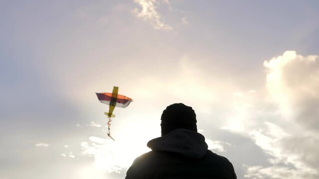 Flying kite on the background of the sky at sunset on a sunny day. A happy family together in the park at sunset flying a kite. The silhouette of a man. A colored plane. Freedom. A toy. Slow motion