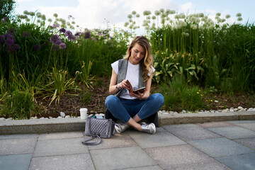 Young female student reading copybook memo notes while learning in city park, Caucasian hipster girl dressed in casual clothes checking information from education textbook have summer vacations