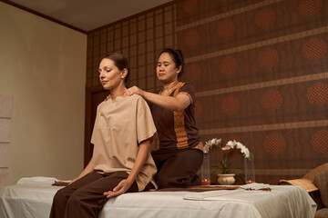 Calm patient massaged in seated position by professional masseuse