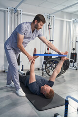 Man lies on floor mat exercising, rehabilitating with elastic band