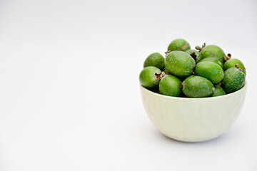 A bowl of green feijoa on the white background on the right of side. Horizontal view.
