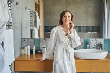 Aged female touching her face and smiling in bathroom