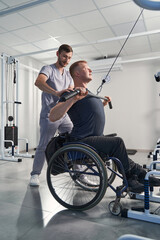 Physical therapist help wheelchair patient in gym. Man with paraplegia