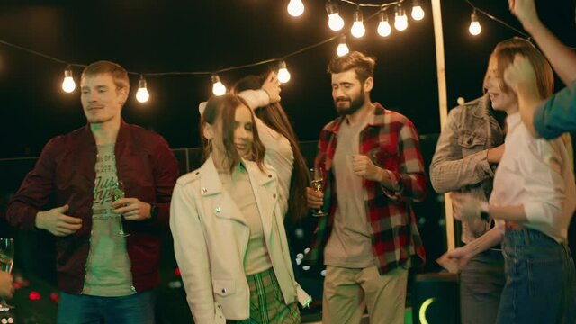 Group of multiracial friends enjoy the night time out on the rooftop of terrace they dancing and taking pictures together