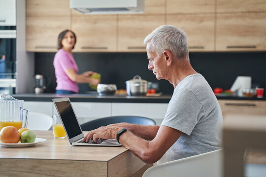 Elderly male in the kitchen sitting in front laptop