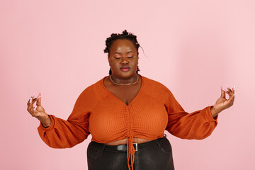 Tranquil black woman with dreadlocks in orange top meditates standing on pastel pink background studio portrait close view